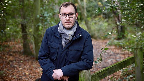 Tom Gordon in woods leaning on a fence post