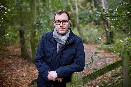 Tom Gordon in woods leaning on a fence post