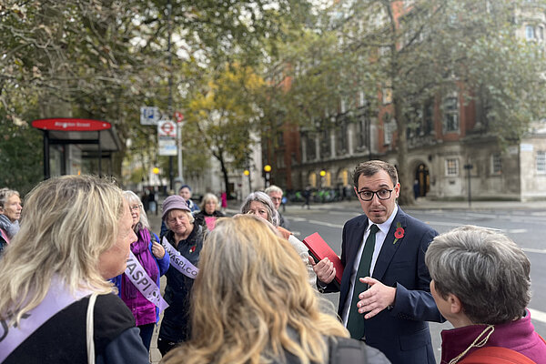 Tom Gordon stood talking to WASPI campaigners by a bus stop near the Houses of Parliament in London