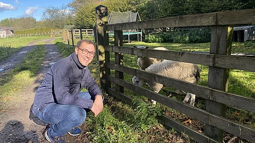 Tom Gordon in a field crouched next to a sheep in a pen