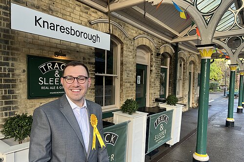 Tom Gordon stood in front of a station sign at Knaresborough Station