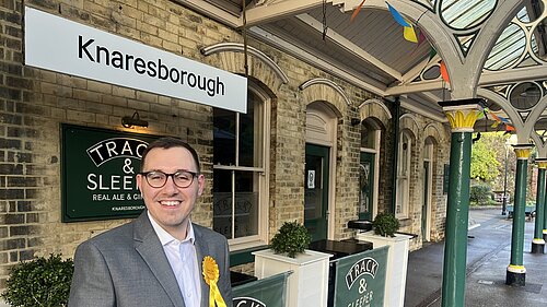 Tom Gordon stood in front of a station sign at Knaresborough Station