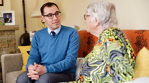 Tom Gordon sat on a sofa talking to a pensioner